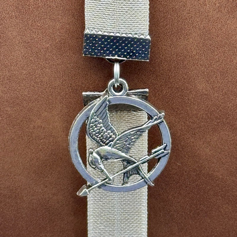 A silver Hunger Games Mockingjay charm on an elastic Bookband