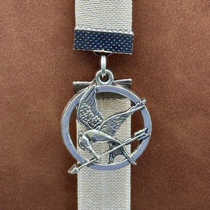A silver Hunger Games Mockingjay charm on an elastic Bookband