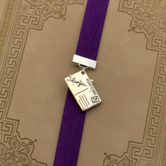 A silver postcard charm on an elastic Bookband