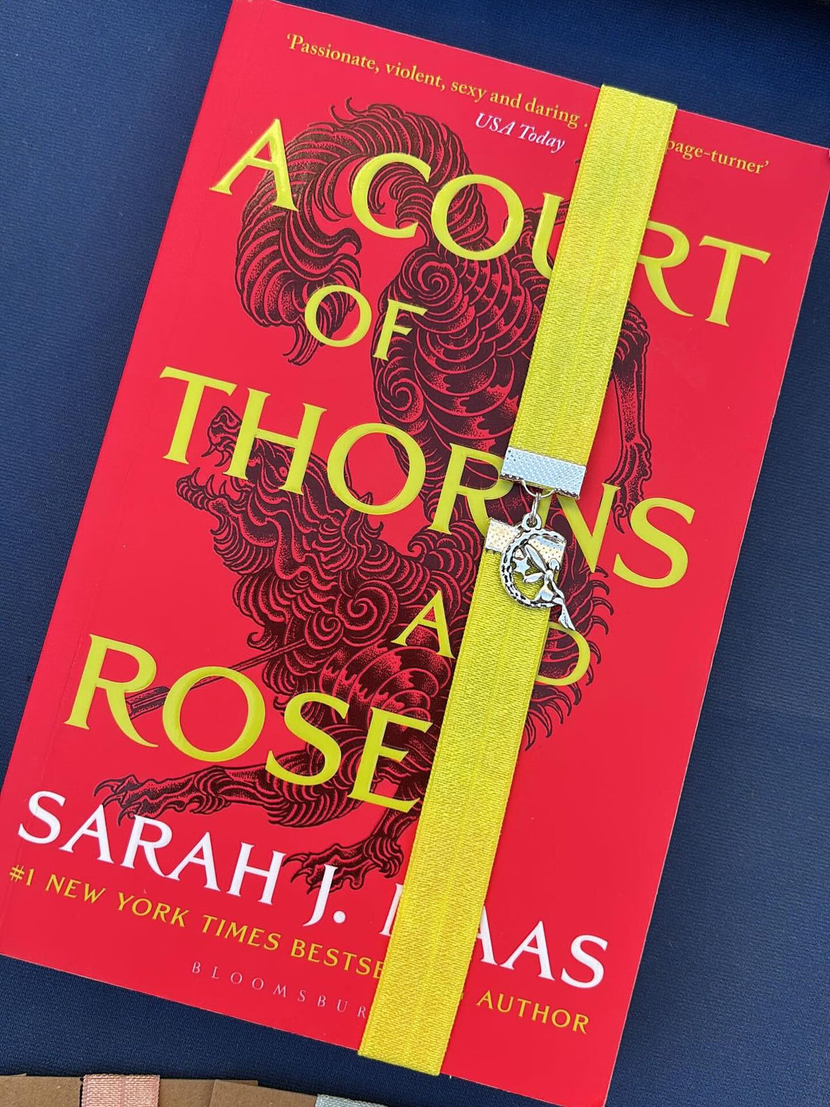 Book titled 'A Court of Thorns and Rose' by Sarah J. Maas with a yellow elastic bookband bookmark