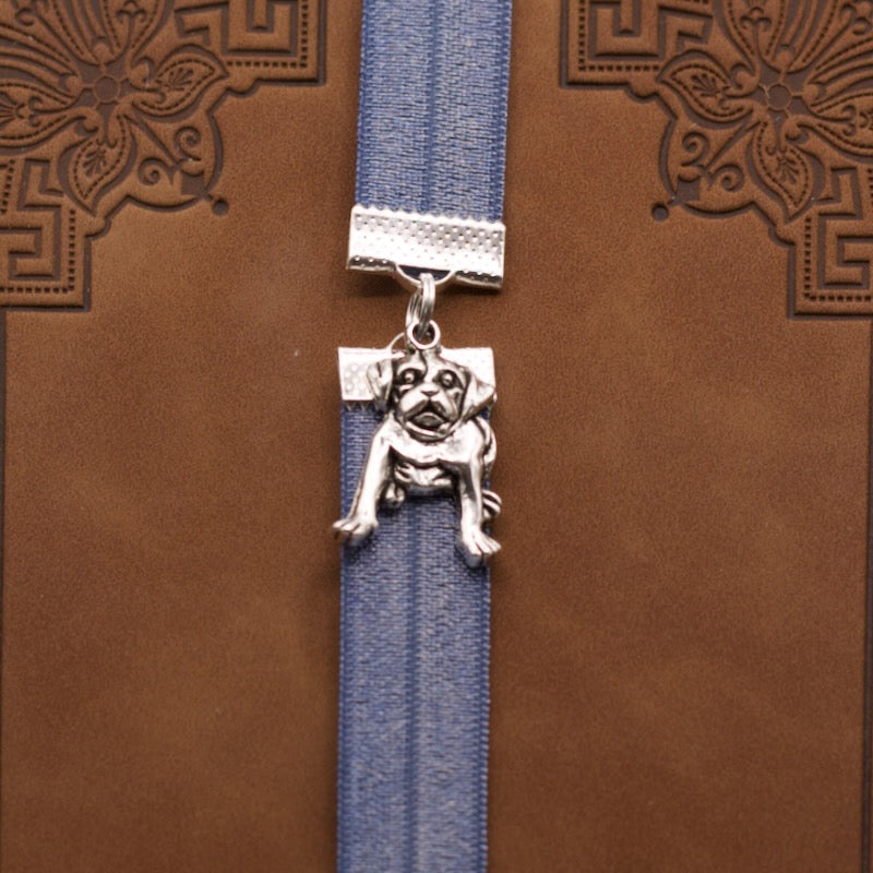 Bookband elastic bookmark with a silver dog design on a metallic blue ribbon on a brown book