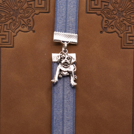 Bookband elastic bookmark with a silver dog design on a metallic blue ribbon on a brown book